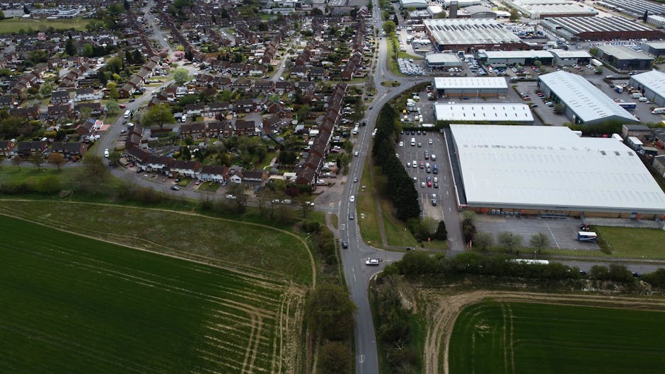Aerial view of a residential property showing a narrow driveway with a red and white removals van parked at the entrance, adjacent to neatly mowed green lawns and surrounding mature trees. The propert